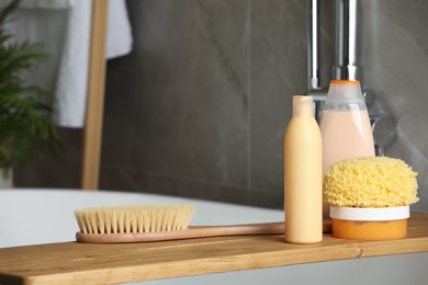 Photo of Wooden bath tray with shampoo, conditioner and other toiletries on tub indoors