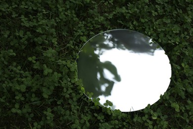 Photo of Round mirror among clovers reflecting tree and sky. Space for text