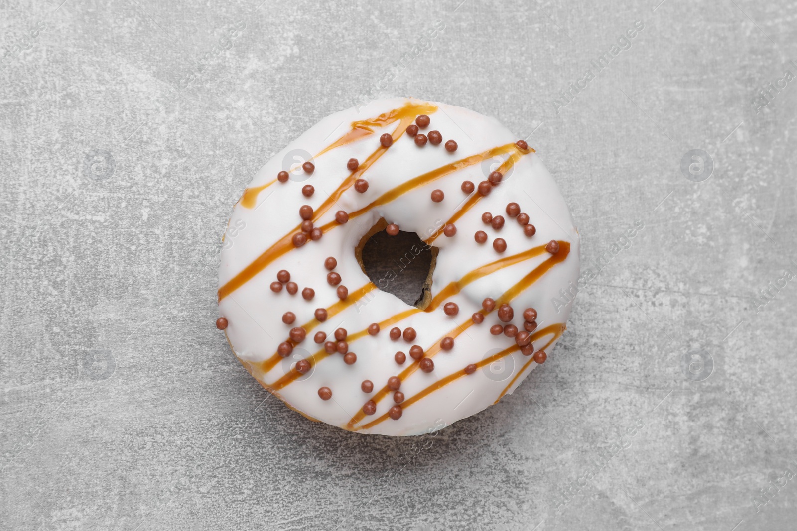 Photo of Tasty glazed donut decorated with sprinkles on light grey table, top view
