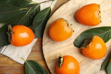Photo of Delicious fresh persimmons and green leaves on wooden table, flat lay
