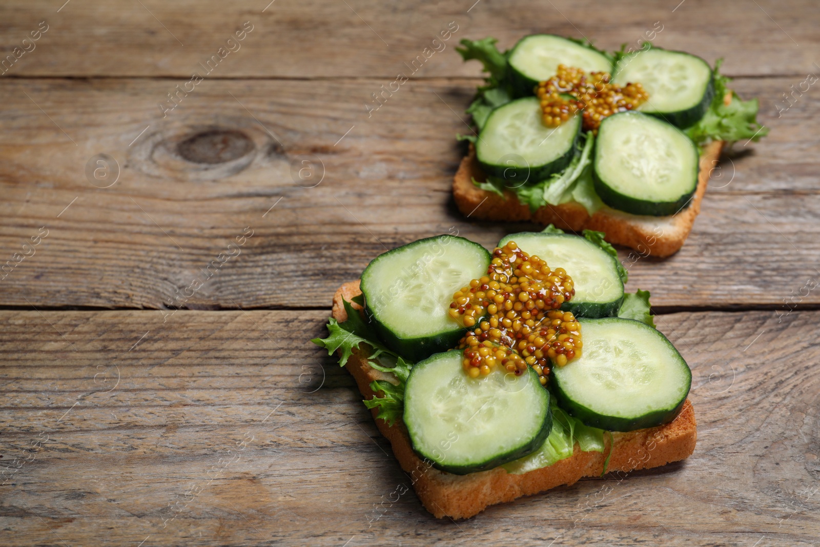 Photo of Tasty cucumber sandwiches with arugula and mustard on wooden table, space for text