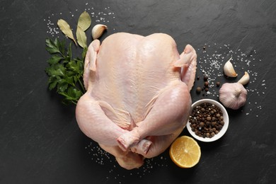 Photo of Fresh raw chicken with spices and lemon on black textured table, flat lay