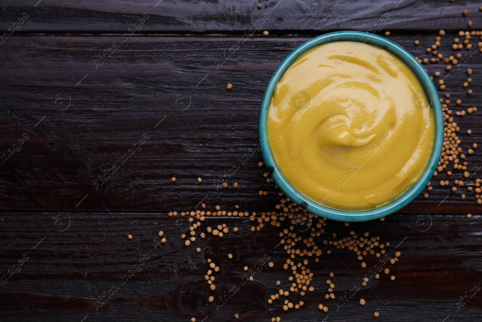 Photo of Sauce bowl with delicious mustard and seeds on dark wooden table, flat lay. Space for text