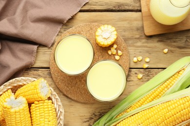 Photo of Tasty fresh corn milk in glasses and cobs on wooden table, flat lay
