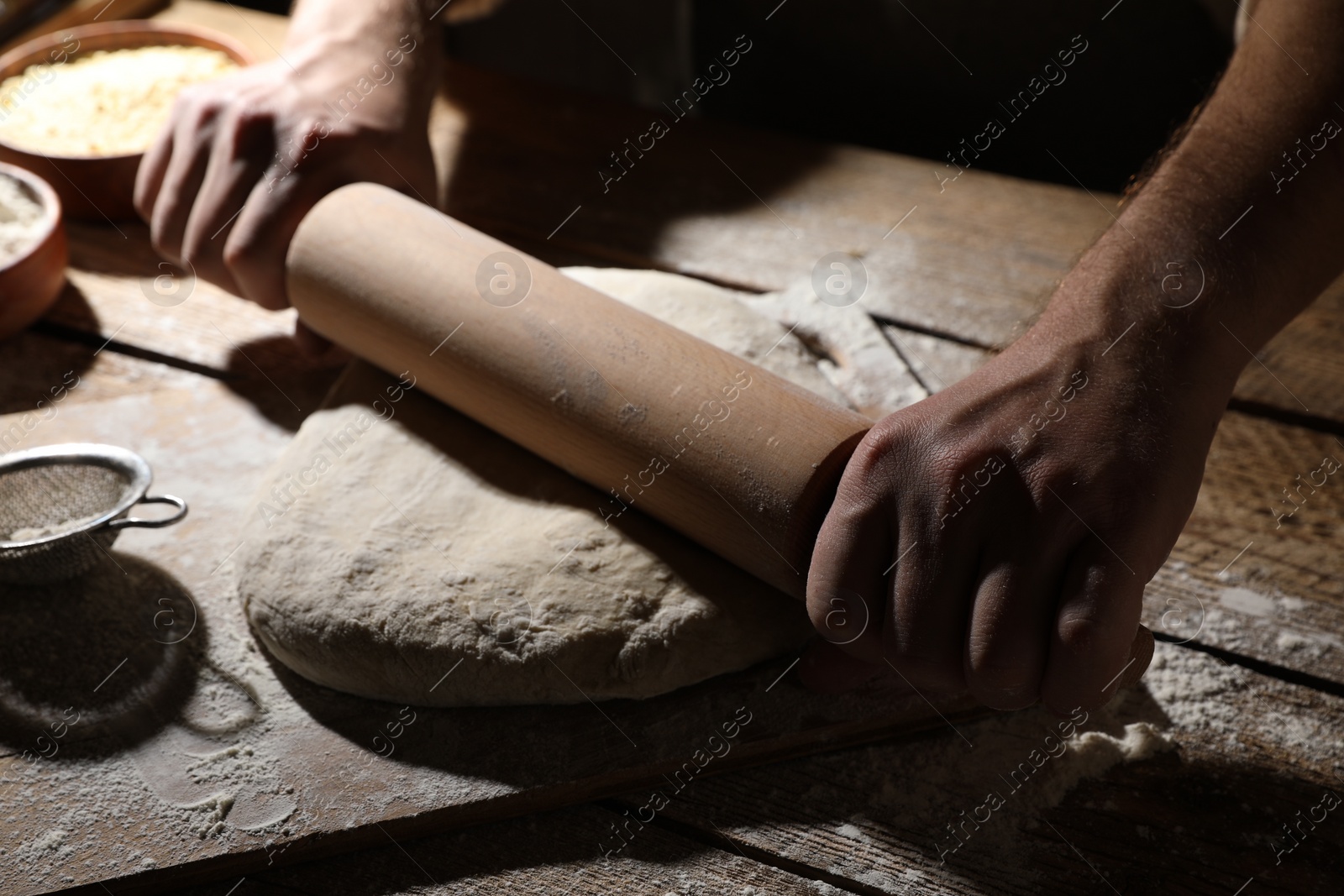Photo of Man rolling raw dough at wooden table, closeup