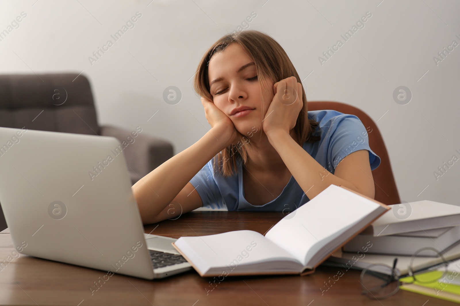 Photo of Young tired woman sleeping near books at wooden table indoors