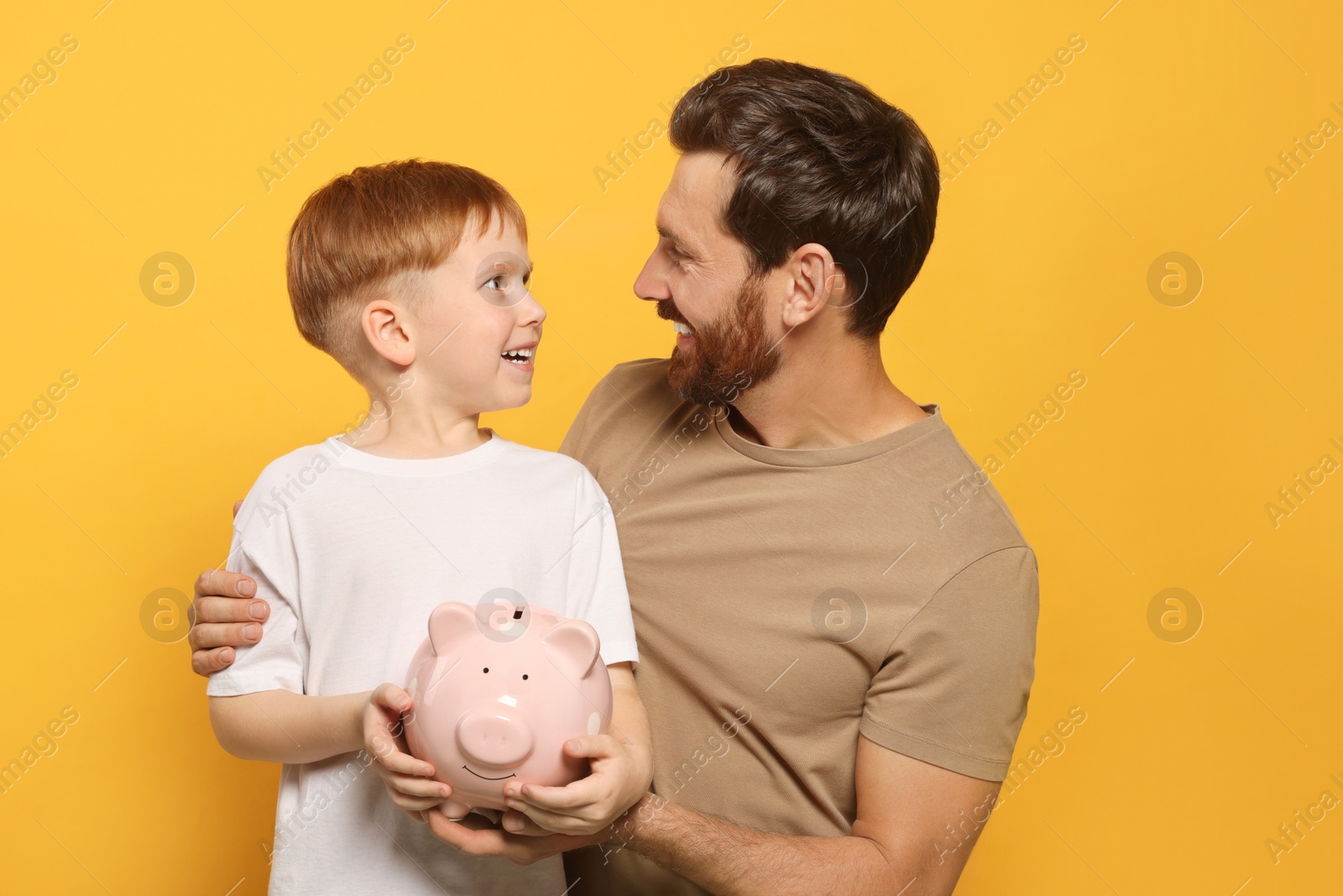 Photo of Father and his son with ceramic piggy bank on orange background