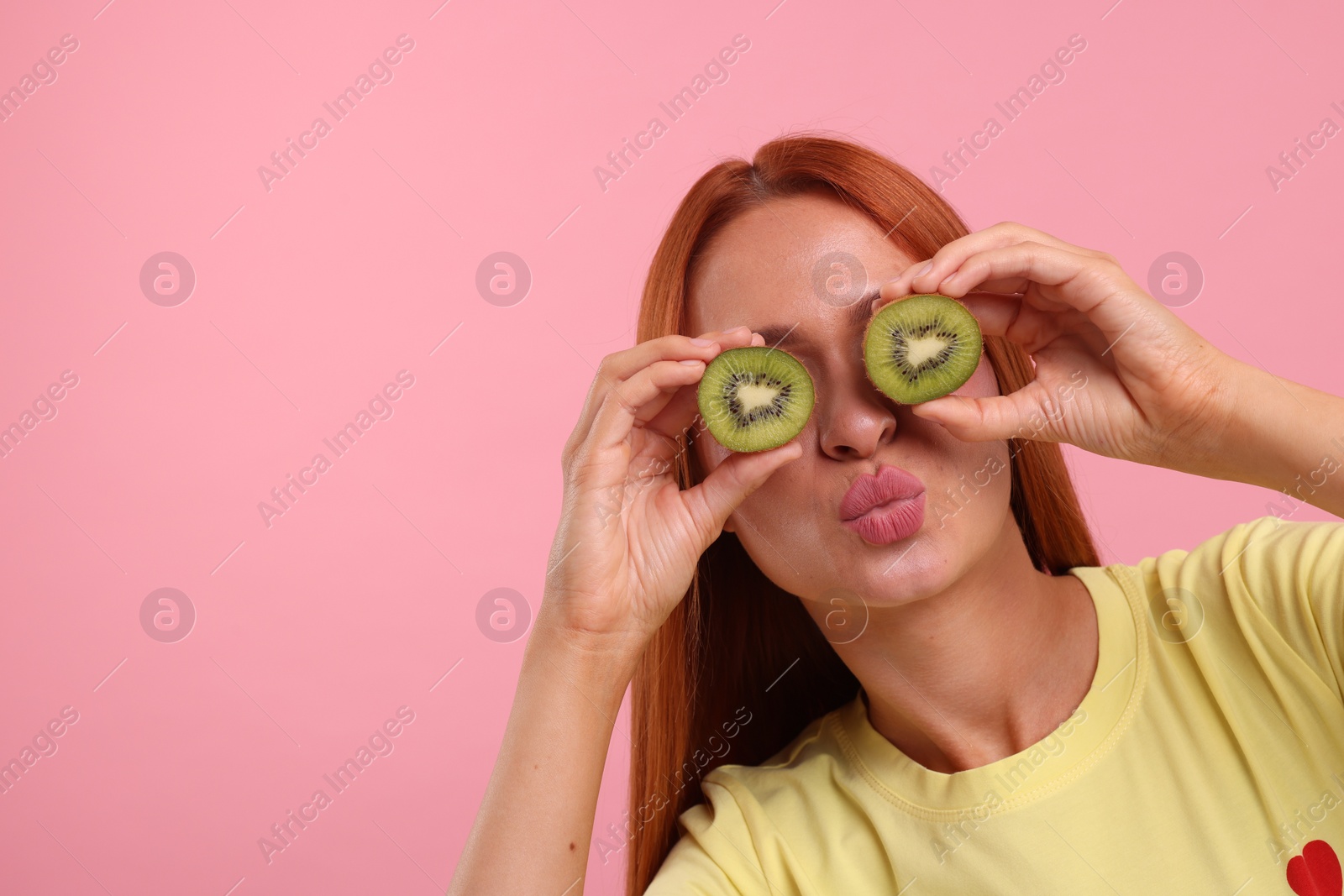 Photo of Funny woman covering eyes with halves of fresh kiwi on pink background, space for text