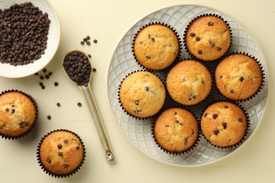 Delicious sweet muffins with chocolate chips on beige wooden table, flat lay