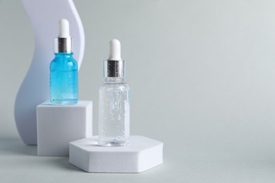 Presentation of bottles with cosmetic serums on light grey background, space for text