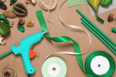 Photo of Hot glue gun and handicraft materials on brown background, flat lay