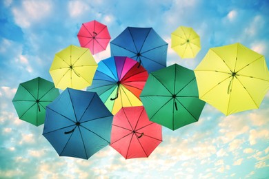 Image of Group of different colorful umbrellas against blue sky with white clouds on sunny day, bottom view