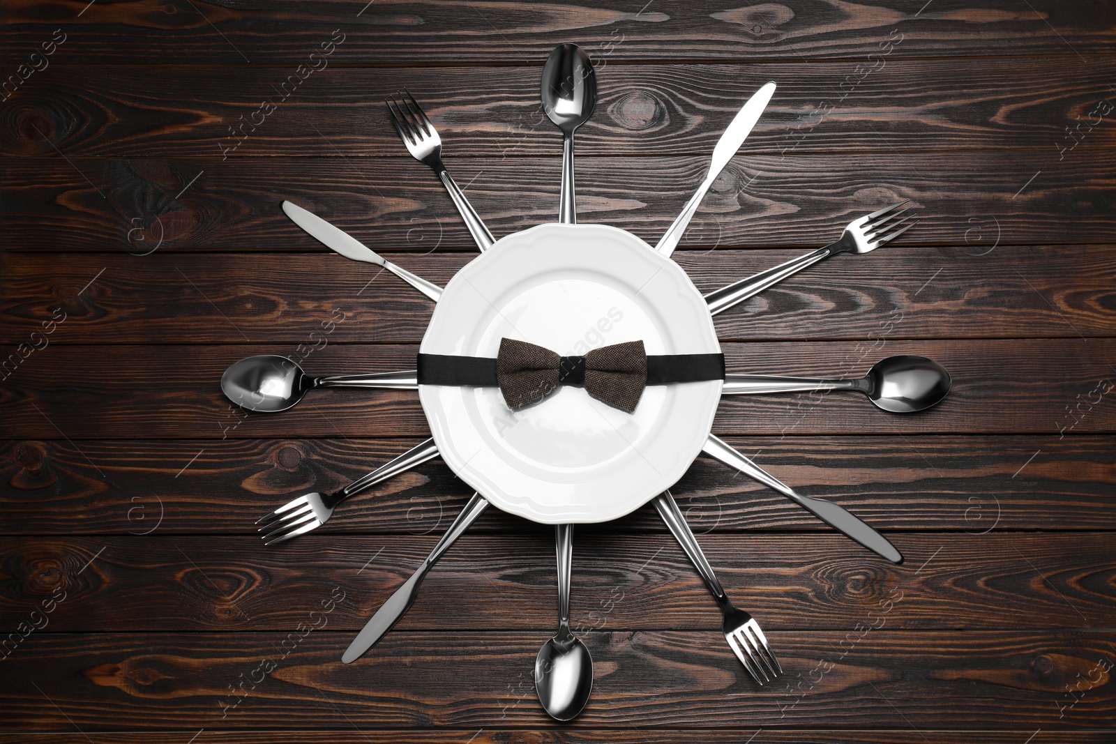 Photo of Business lunch concept. Plate with bow tie and cutlery on wooden table, flat lay