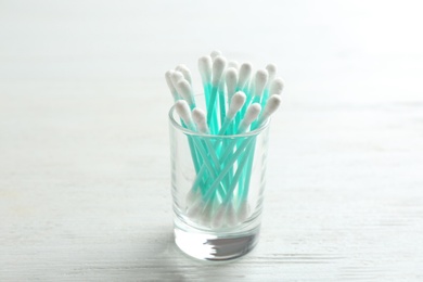 Glass with cotton swabs on white wooden background