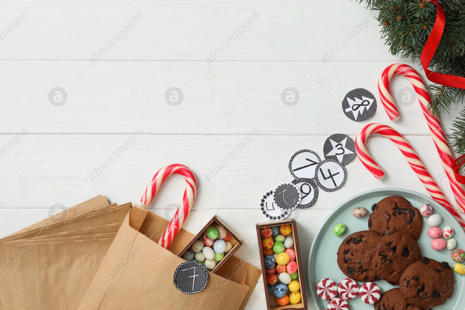 Photo of Flat lay composition with paper bags and Christmas treats on white wooden table, space for text. Creating advent calendar