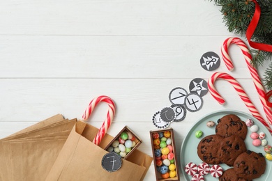 Flat lay composition with paper bags and Christmas treats on white wooden table, space for text. Creating advent calendar