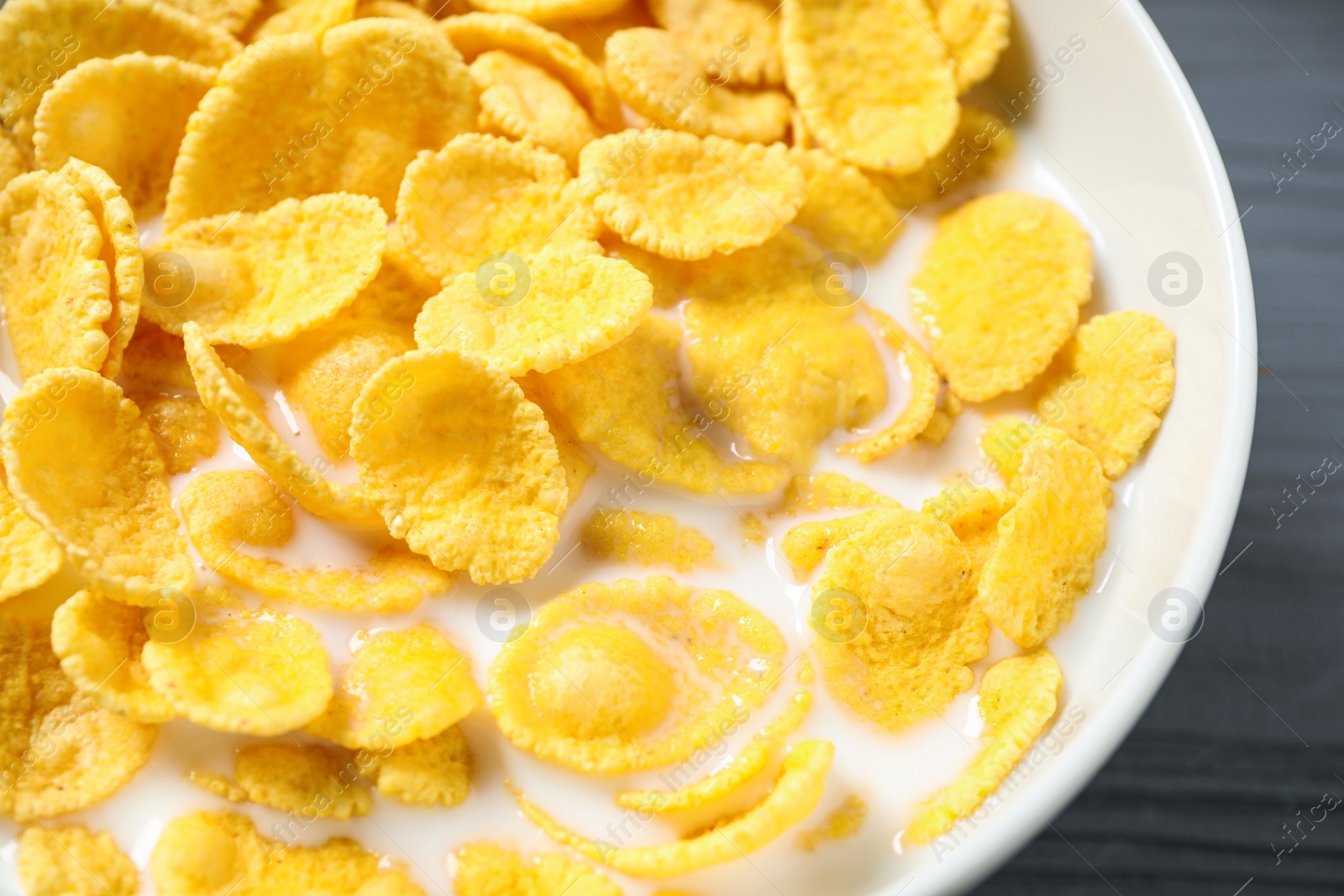 Photo of Tasty crispy corn flakes with milk in bowl, closeup
