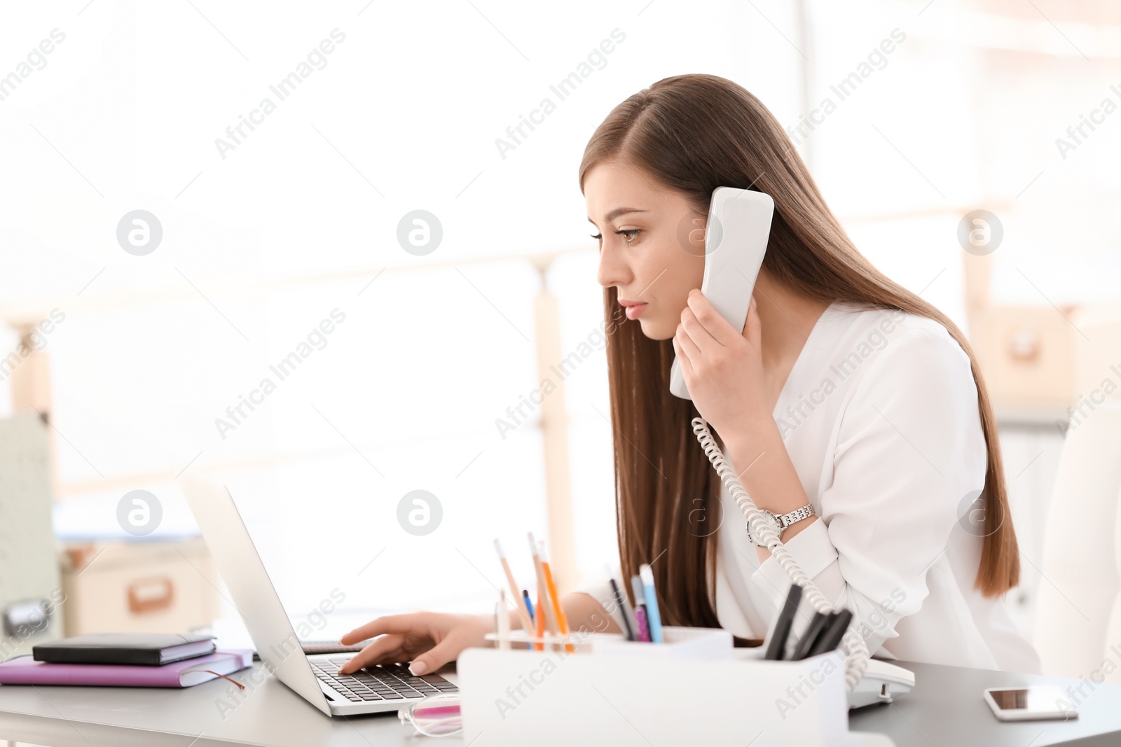 Photo of Young woman talking on phone at workplace