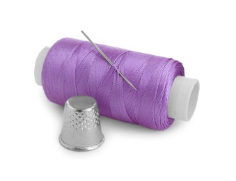 Photo of Thimble and spool of violet sewing thread with needle isolated on white