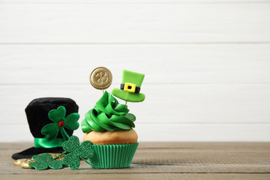 Photo of Decorated cupcake and hat on wooden table, space for text. St. Patrick's Day celebration