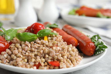 Photo of Tasty buckwheat porridge with sausages and vegetables on table, closeup