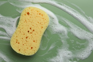 Yellow sponge with foam on green background, top view