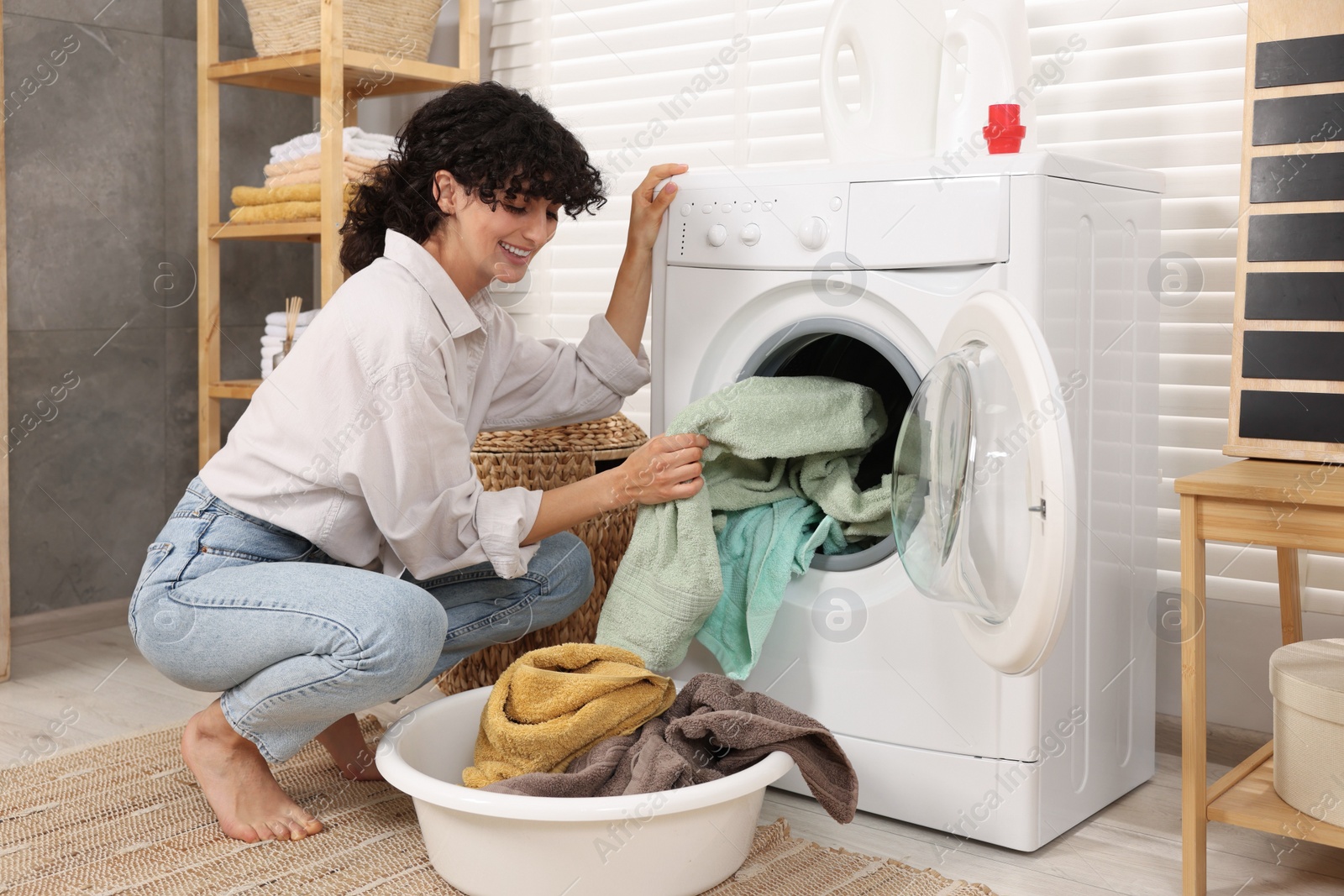 Photo of Woman taking laundry out of washing machine indoors