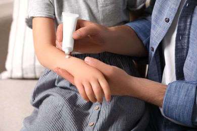 Photo of Father applying ointment onto his daughter's arm on couch, closeup