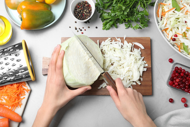 Photo of Woman making cabbage salad at light grey table, top view