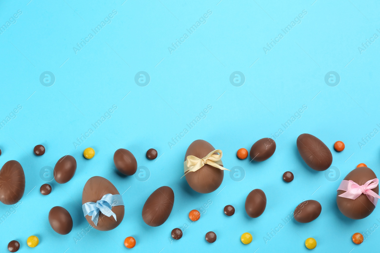 Photo of Sweet chocolate eggs and bright candies on light blue background, flat lay. Space for text