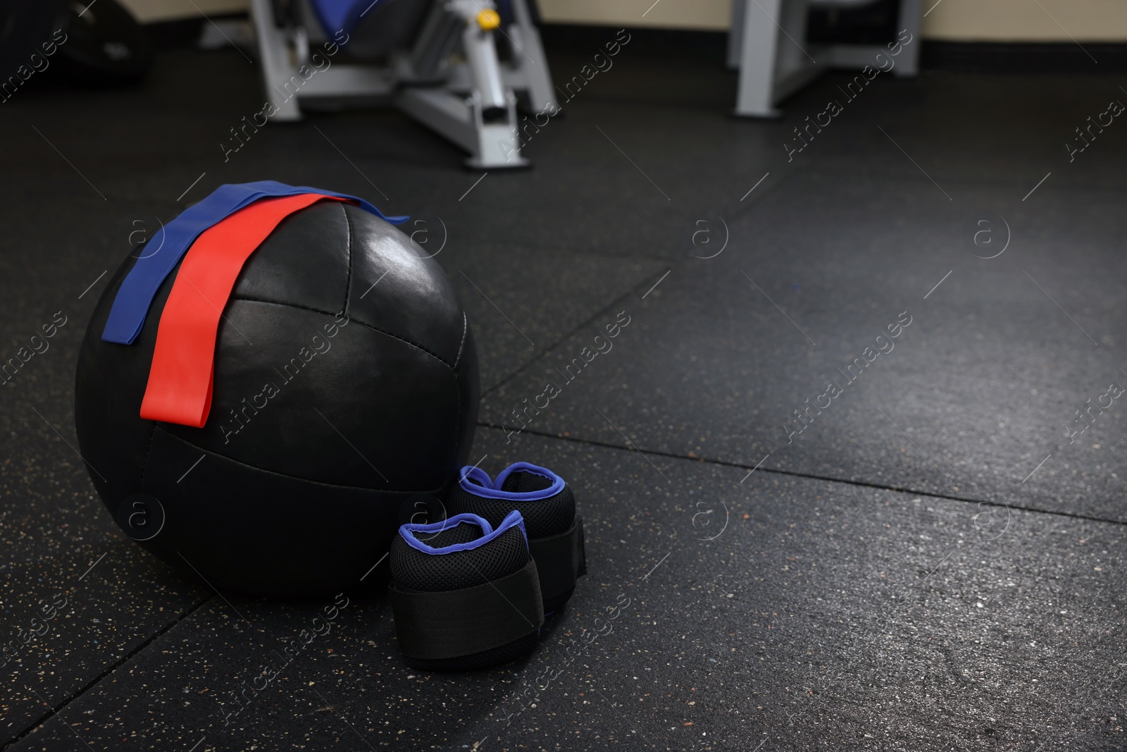 Photo of Black medicine ball, elastic bands and weighting agents on floor in gym, space for text