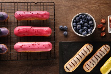 Photo of Different tasty glazed eclairs, dry strawberries and blueberries on wooden table, flat lay