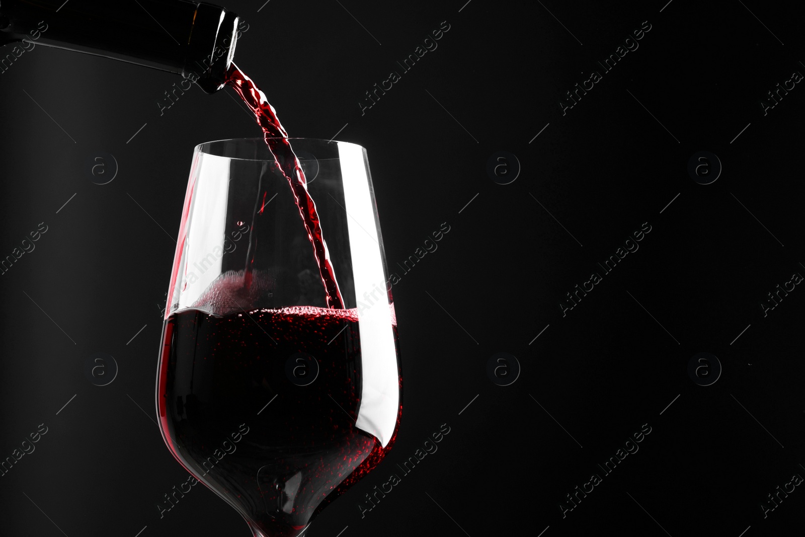 Photo of Pouring red wine into glass against black background, closeup. Space for text