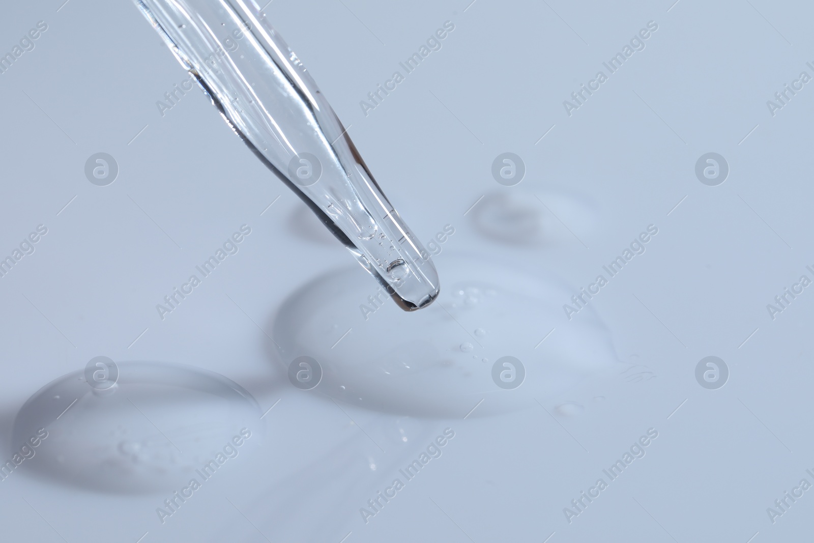 Photo of Glass pipette and transparent liquid on white background, closeup