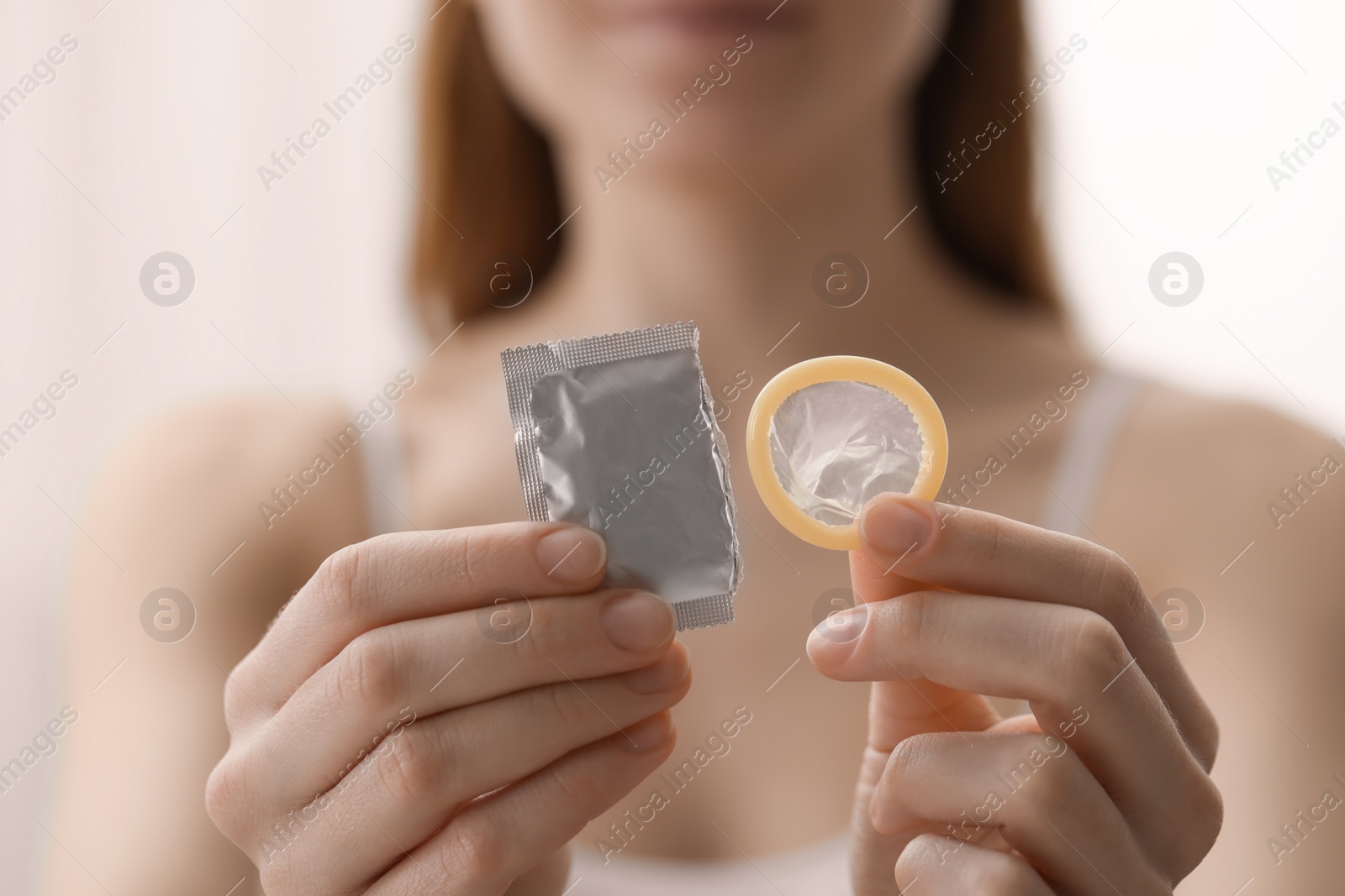 Photo of Woman holding unwrapped condom indoors, closeup. Safe sex