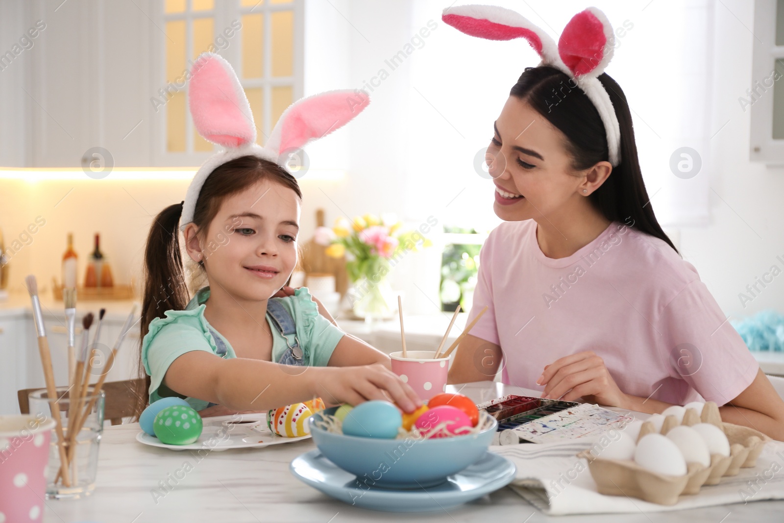 Photo of Happy mother with her cute daughter painting Easter eggs at table in kitchen