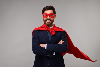 Happy businessman wearing red superhero cape and mask on beige background