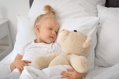 Cute little girl with teddy bear sleeping in bed