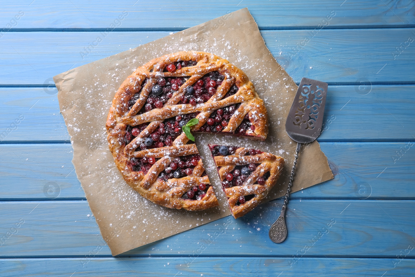 Photo of Delicious cut currant pie with fresh berries and spatula on blue wooden table, flat lay