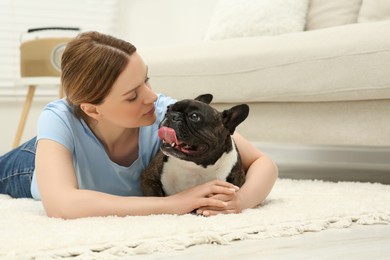 Photo of Woman hugging cute French Bulldog on soft carpet in room