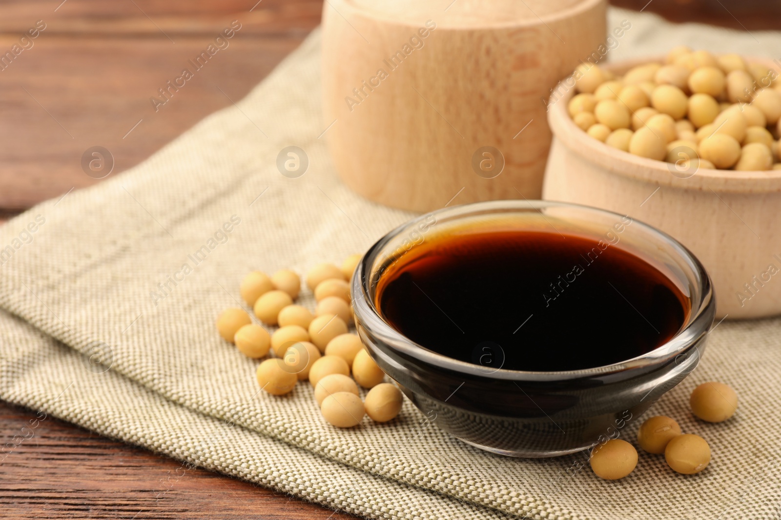 Photo of Soy sauce in bowl and soybeans on wooden table, closeup