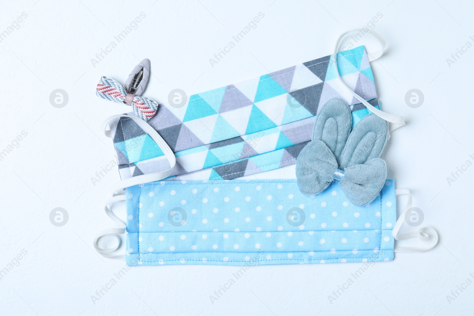 Photo of Homemade protective masks and adorable girly hair clips on white background, flat lay. Sewing for child