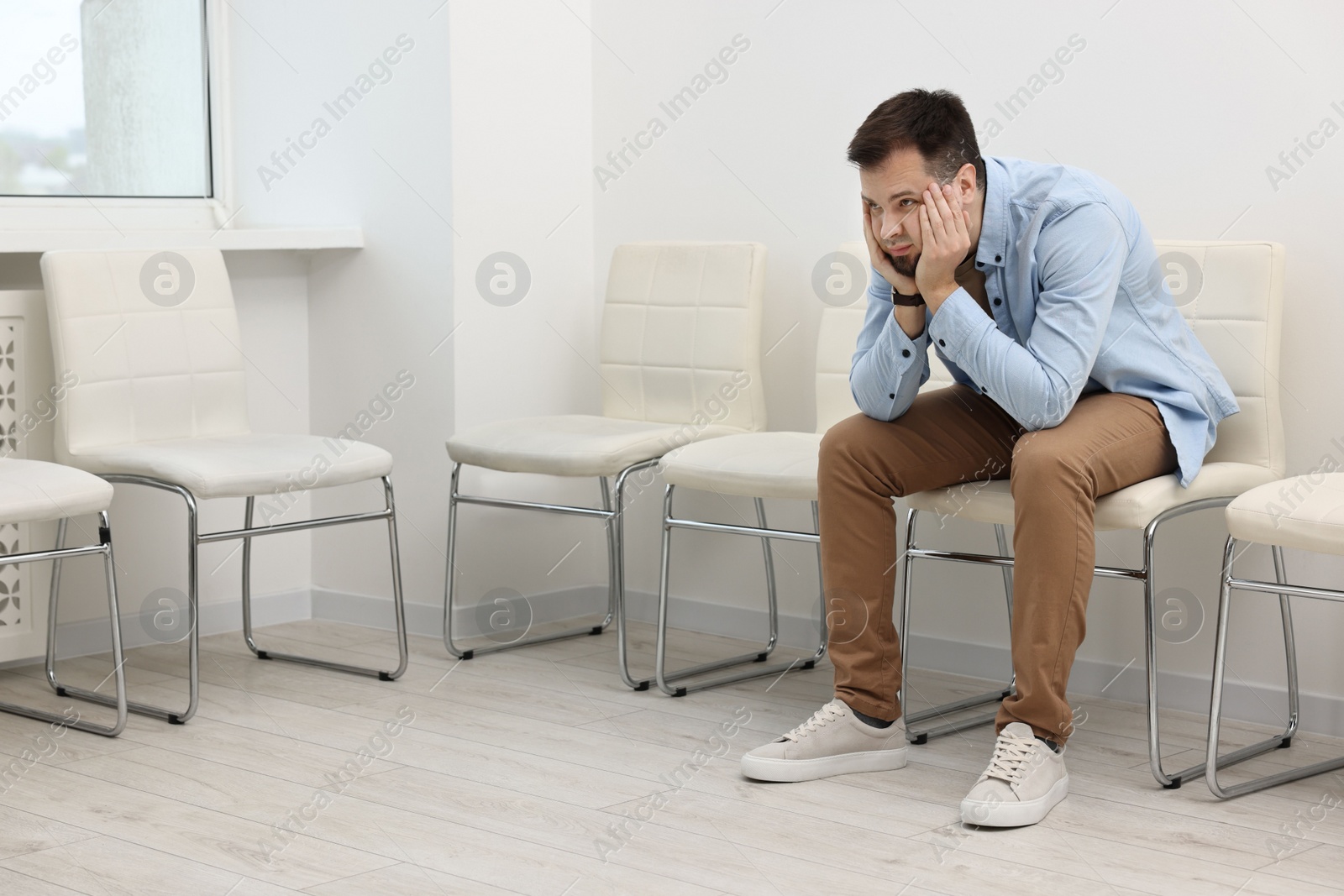 Photo of Man sitting on chair and waiting for appointment indoors