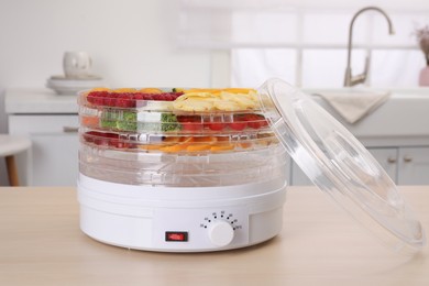 Photo of Cut fruits and vegetables in dehydrator machine on wooden table