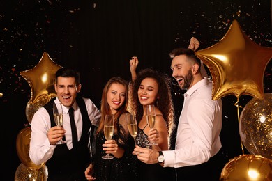 Happy friends with glasses of sparkling wine celebrating New Year on black background