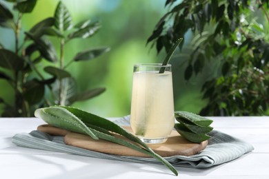 Photo of Fresh aloe juice in glass and leaves on white wooden table outdoors