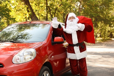 Authentic Santa Claus with bag full of presents near car outdoors