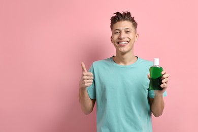 Photo of Young man with mouthwash showing thumbs up on pink background, space for text