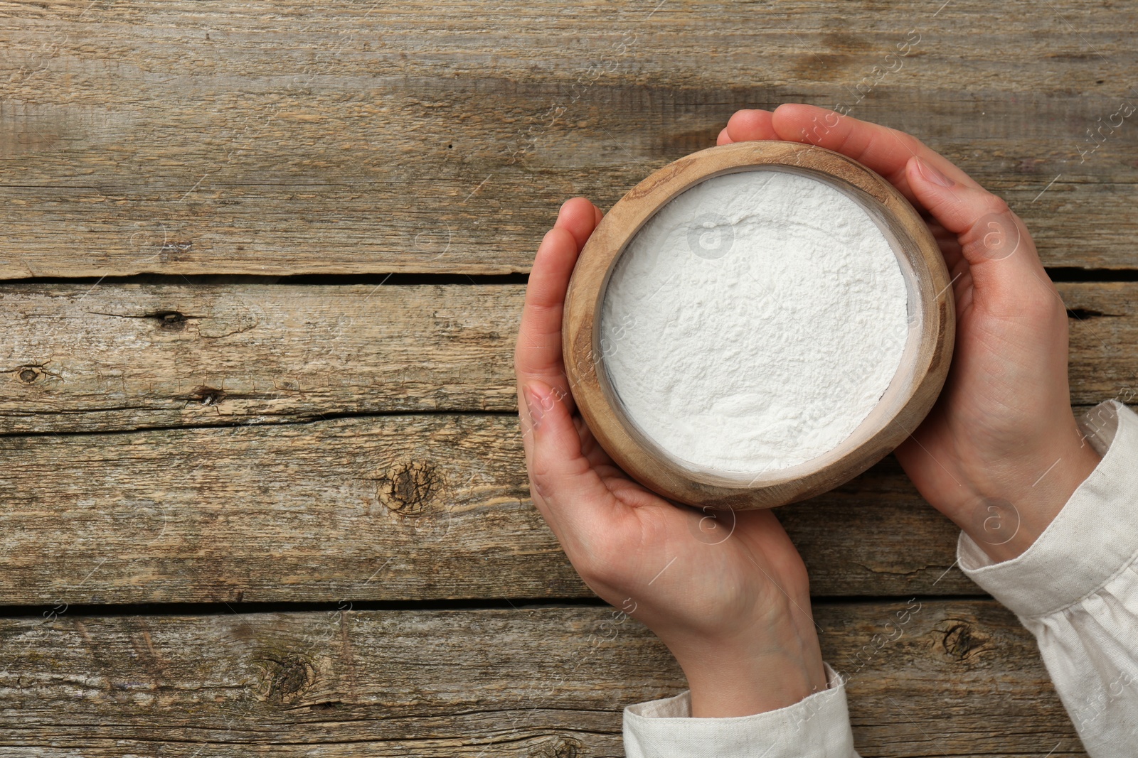 Photo of Woman holding bowl with baking powder at wooden table, top view. Space for text