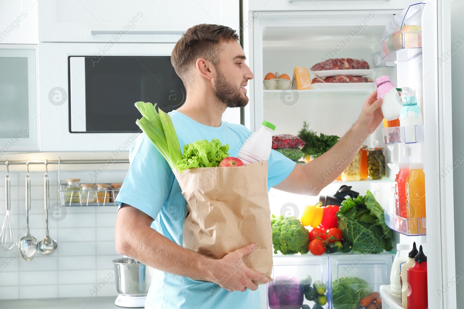 Photo of Man with paper bag putting products into refrigerator in kitchen